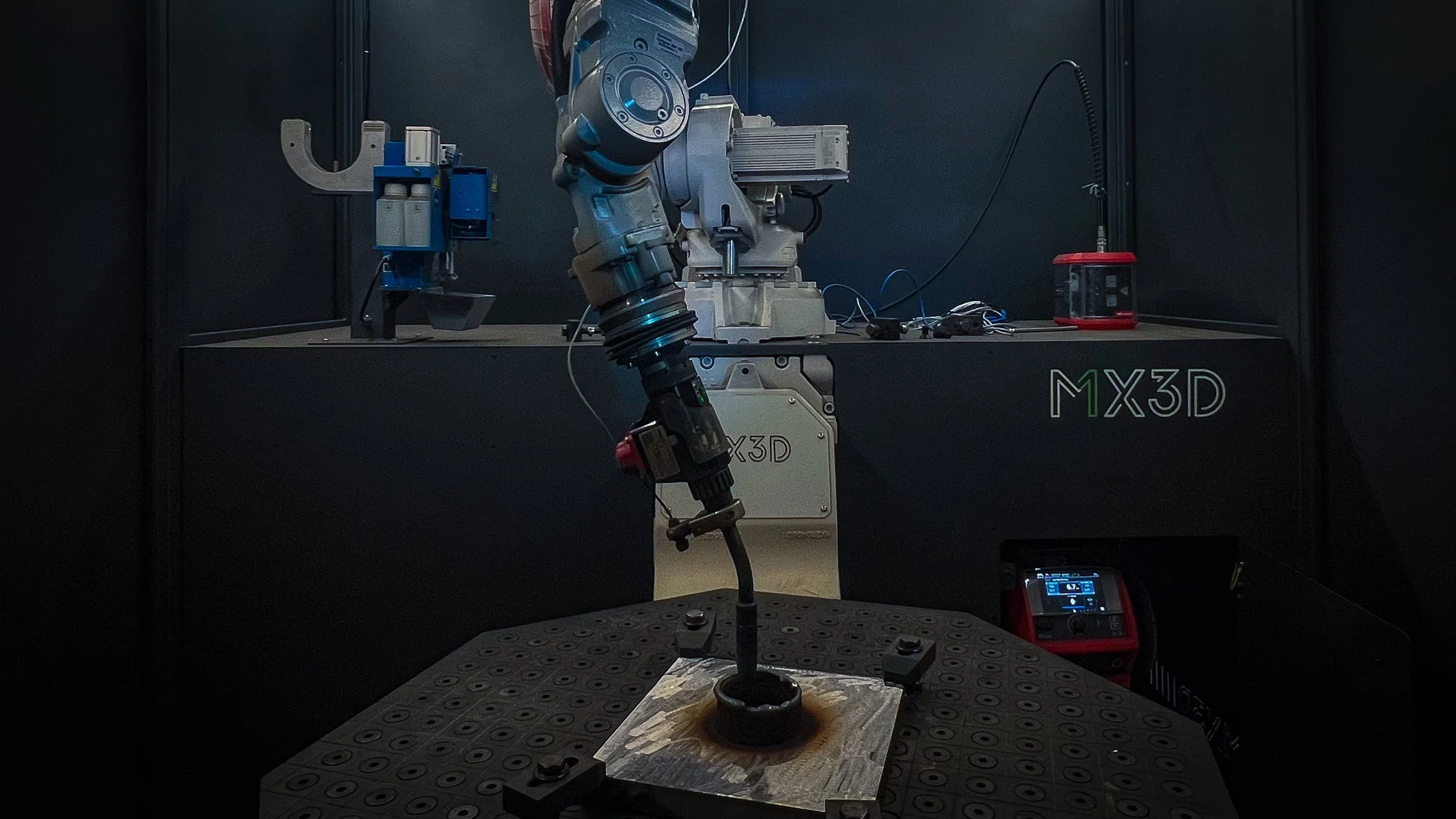 暗い工業環境で、ロボットアームが金属部品に溶接または3Dプリンティングを行っている様子