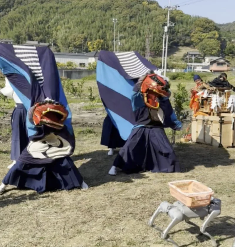 獅子舞を演じる二人のパフォーマーと、バスケットを背負った四足歩行ロボットが共演する屋外イベントの様子。伝統とテクノロジーが融合した日本の祭りの一場面です。