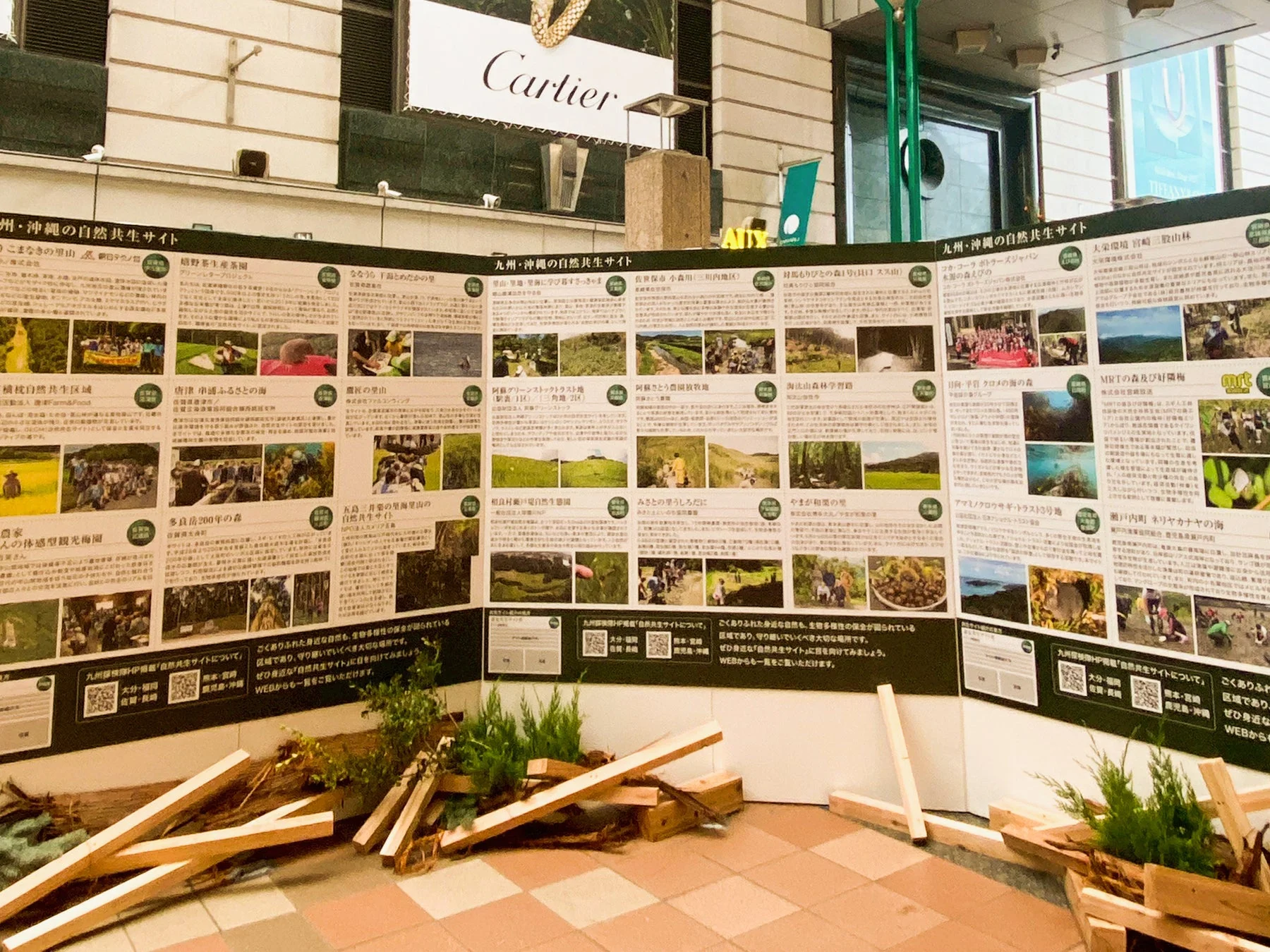 カルティエの看板が見える屋内で、「九州・沖縄の自然共生サイト」に関する大型情報パネルが展示されています。