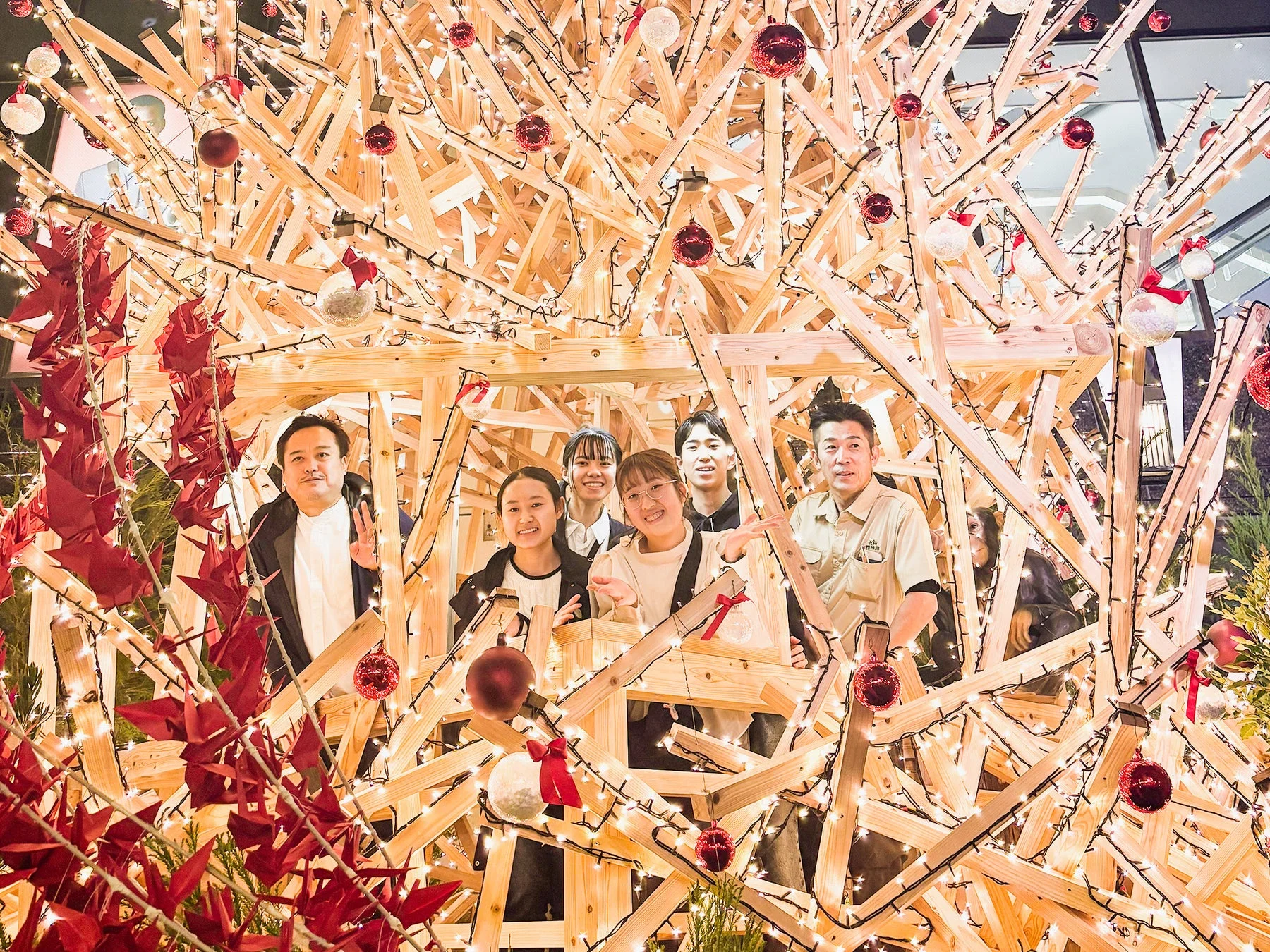 イルミネーションで飾られた木製のオブジェの中に、楽しそうにポーズをとる6人の男女。