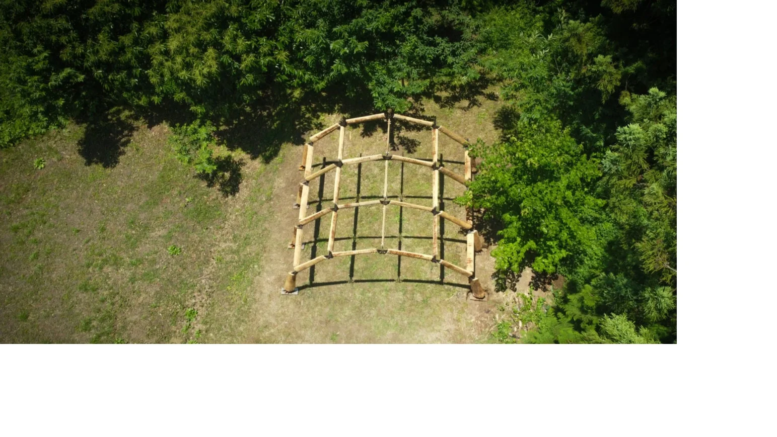 緑豊かな森に囲まれた草地にある木造の骨組みを上空から捉えた画像
