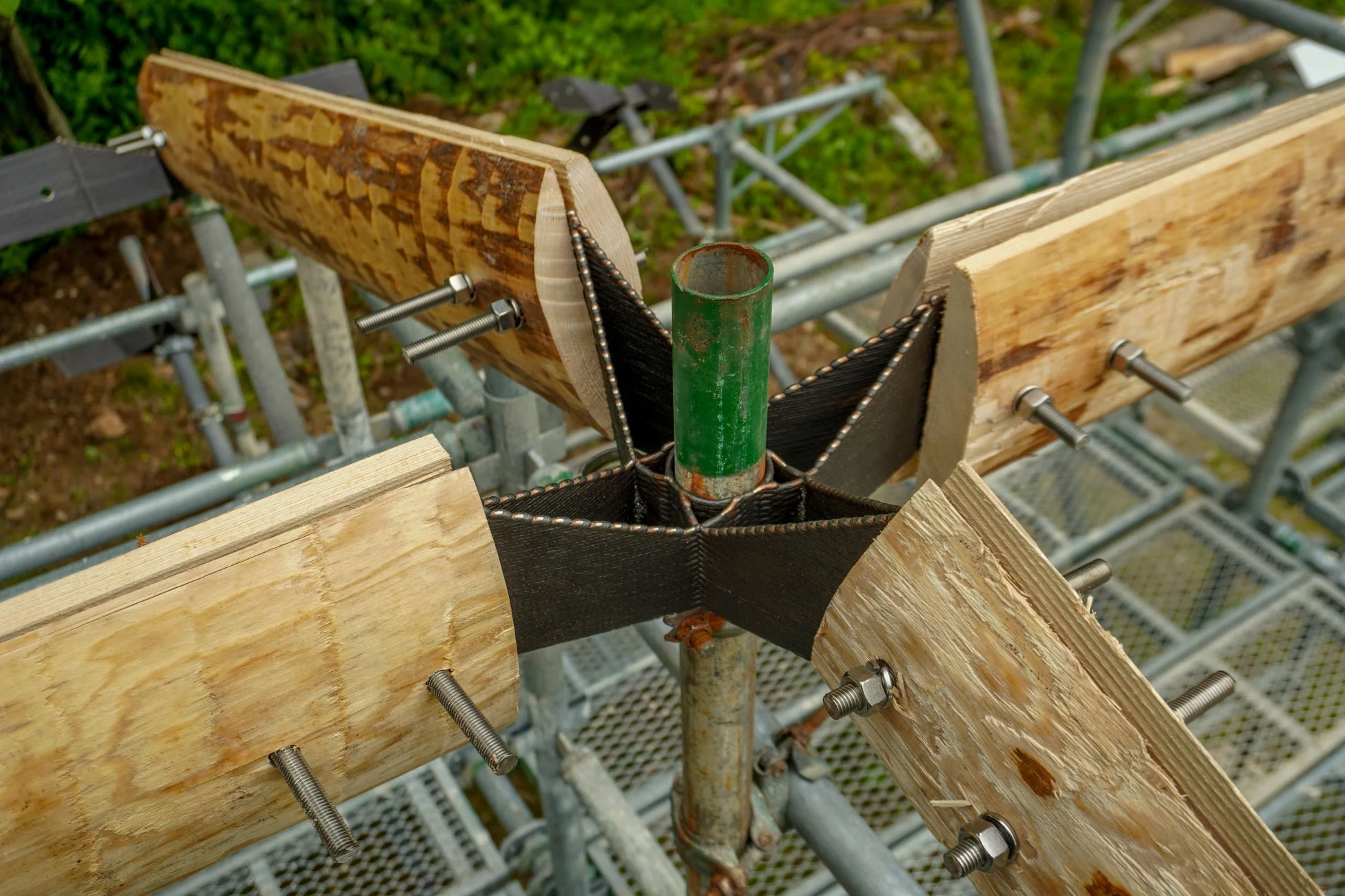 緑色のパイプを中心に、木材と金属製の星形接合部材で構成された建築構造の接続部分