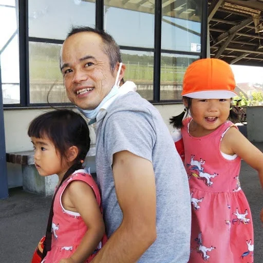 笑顔の男性と2人の幼い女の子が屋外にいる写真