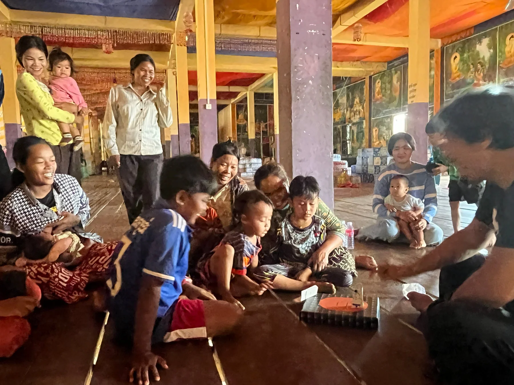 寺院の広間で、多くの大人と子供たちが笑顔で集まり、和やかに交流しています。