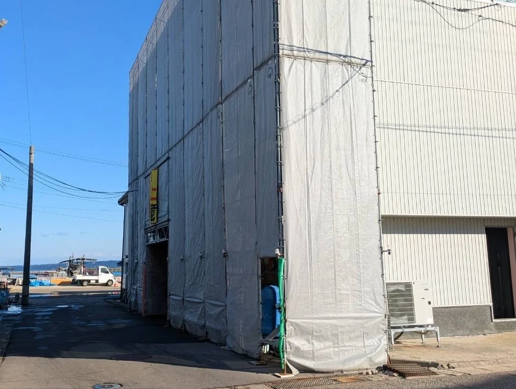 足場と養生シートで覆われた建設中の建物と港の風景