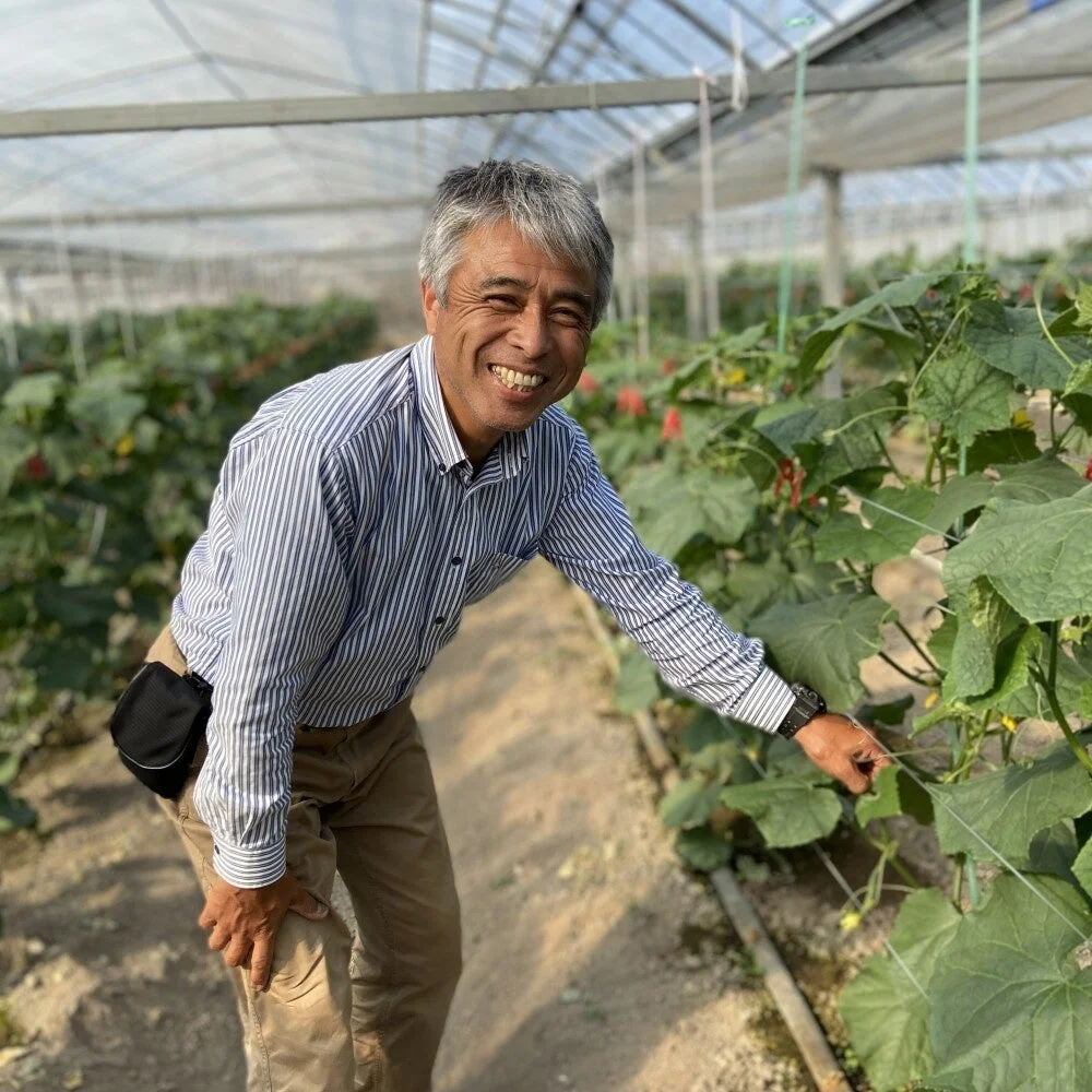 温室の中で笑顔の男性が植物を指差しています