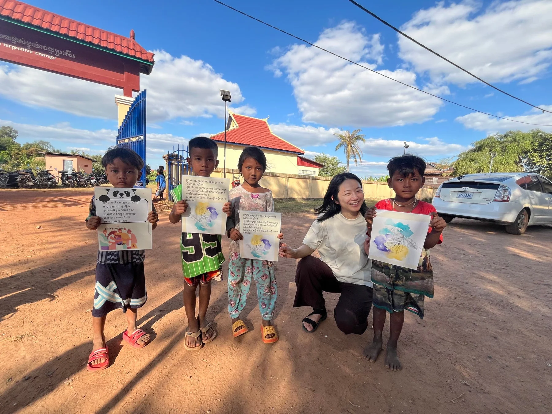 青空の下、アジア人女性が4人の子供たちと笑顔で交流している様子です。