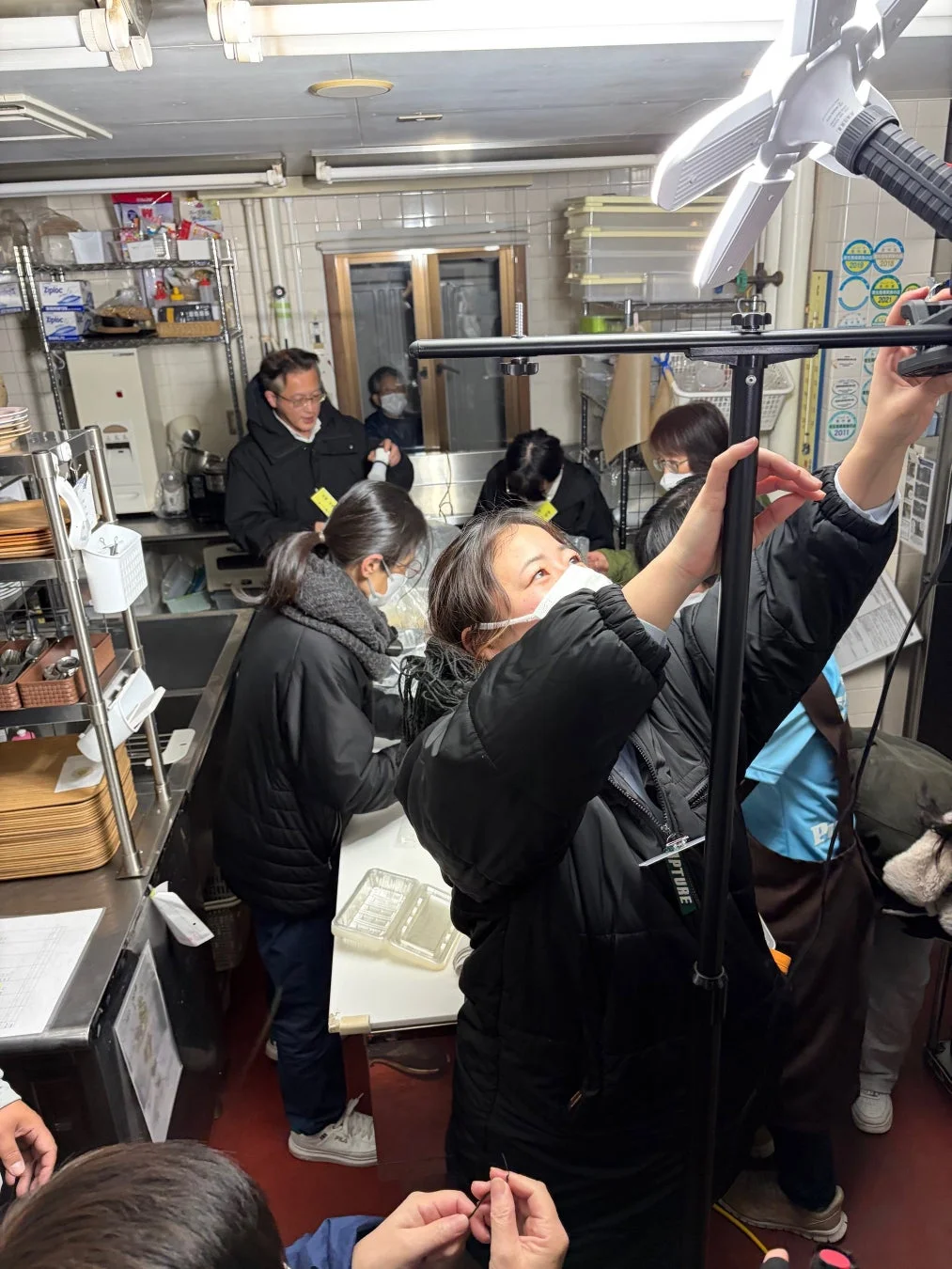 マスクを着用した人々が厨房のような場所で作業している様子