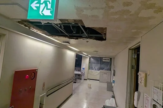 天井が一部崩落し、広範囲に水濡れ跡が見られる廊下の様子