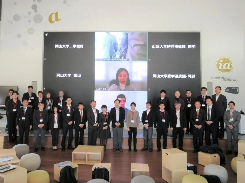 複数の男女が大きなスクリーンを背景に集合写真を撮っています。