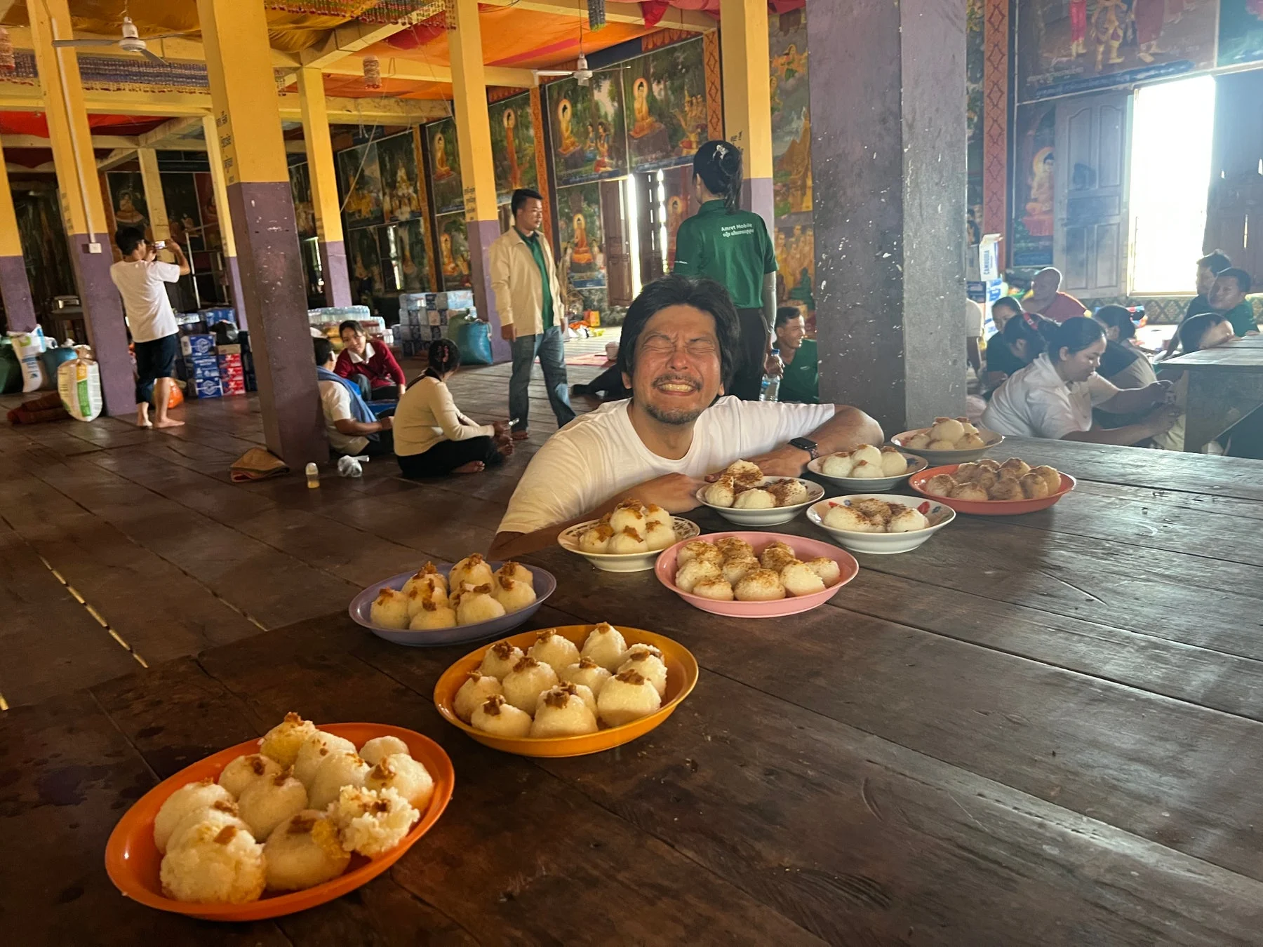 木製のテーブルに並んだお餅のようなデザートを前に、満面の笑みを浮かべる男性。