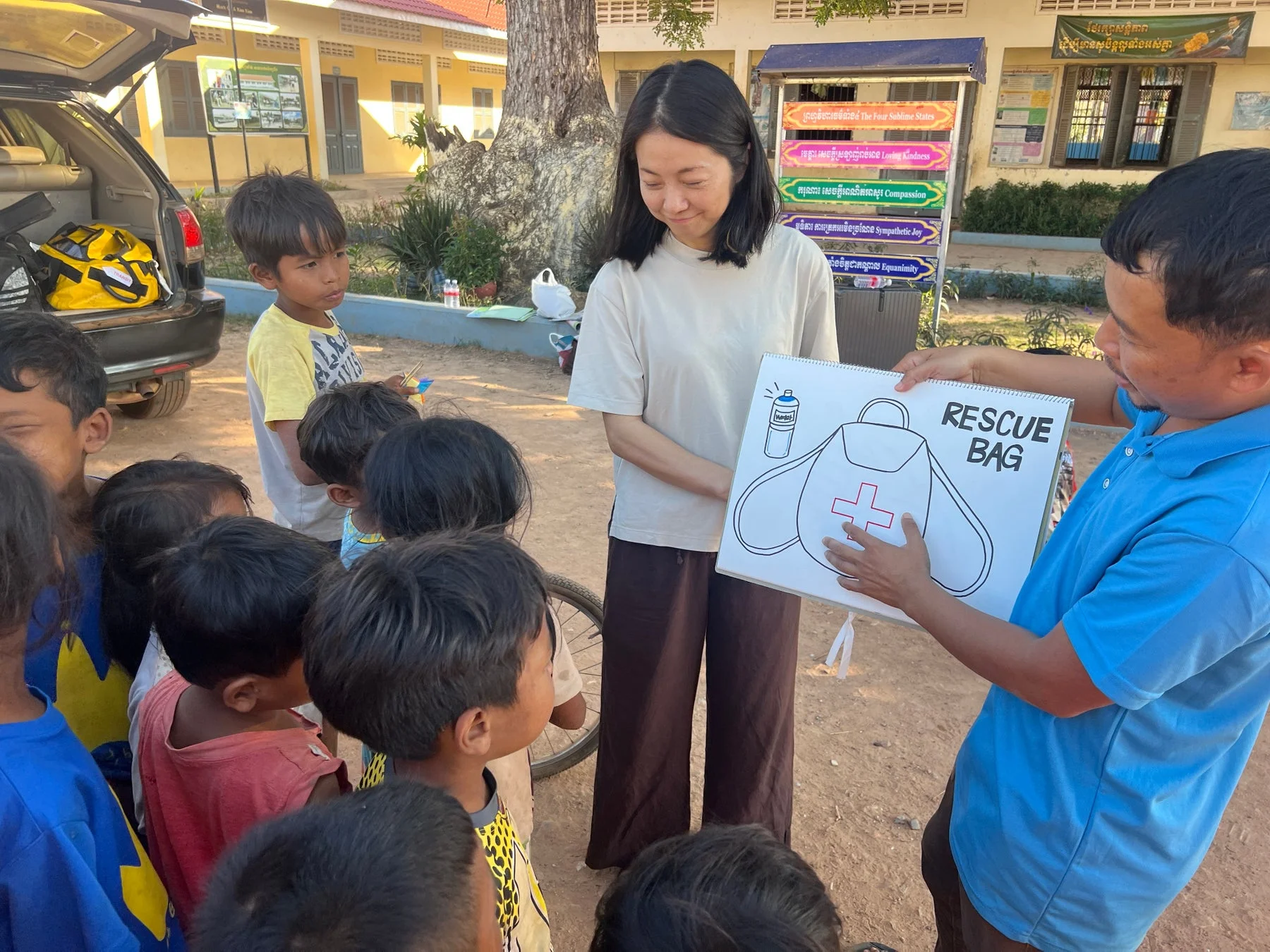 屋外で、大人たちが子供たちに災害準備について教えている様子です。