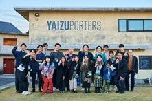 「YAIZU PORTERS」と書かれた建物の前で、笑顔でポーズをとる大勢の男女の集合写真