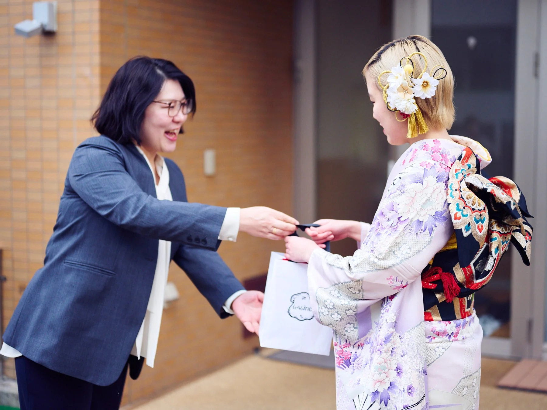 ビジネススーツの女性が着物姿の女性にプレゼントを手渡している様子