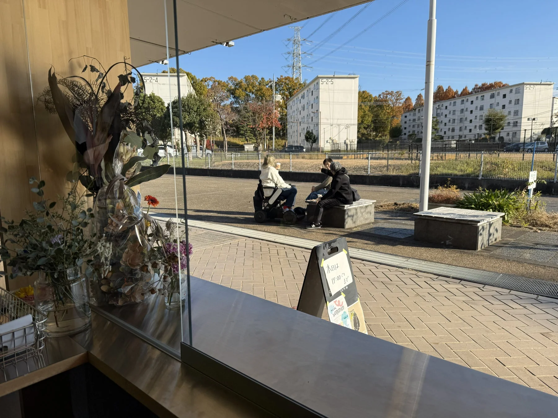 屋外のベンチで会話する二人。一人は車椅子に乗っている。