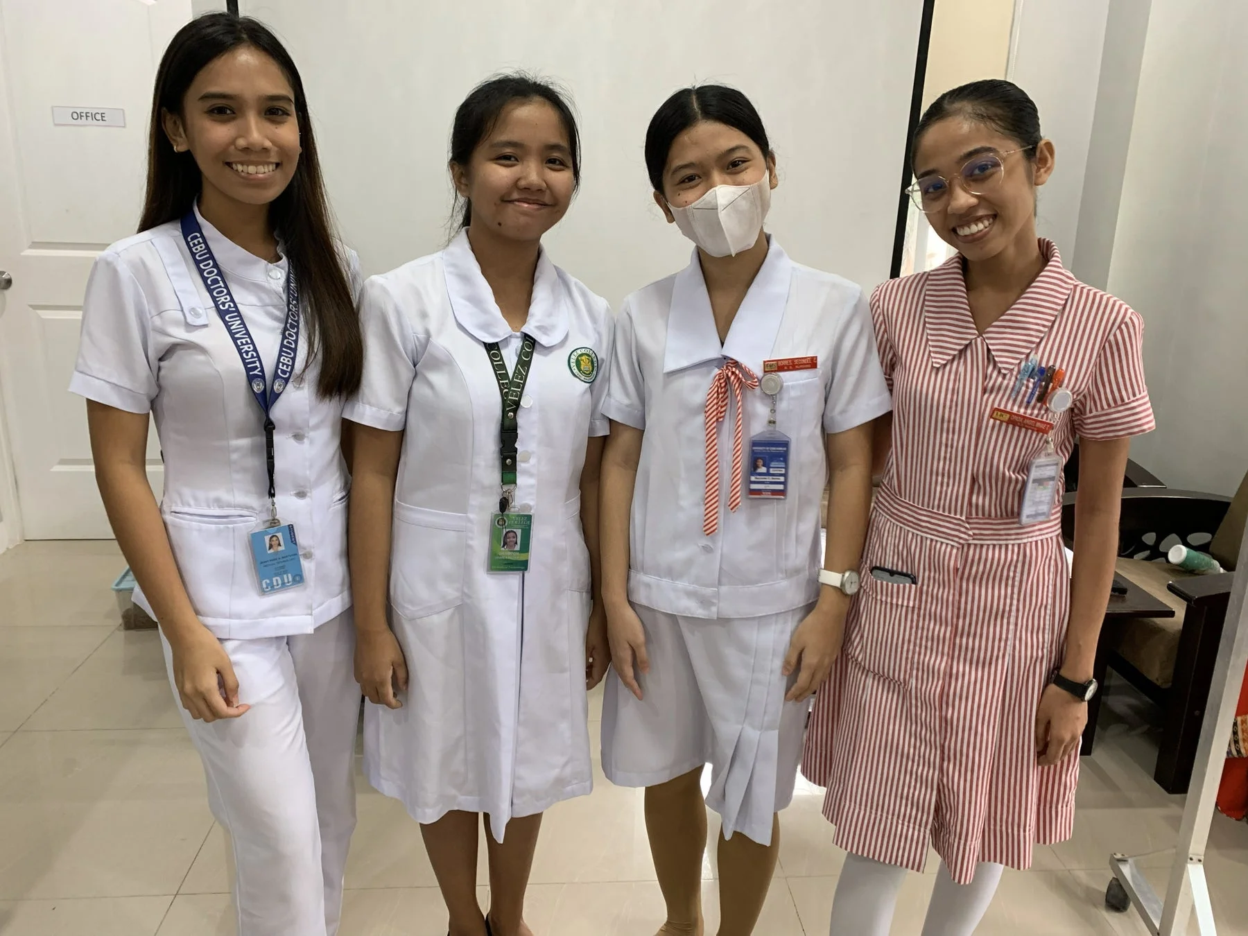 医療系の制服と思われる服装で笑顔で並んで立っている4人の若い女性の写真です。