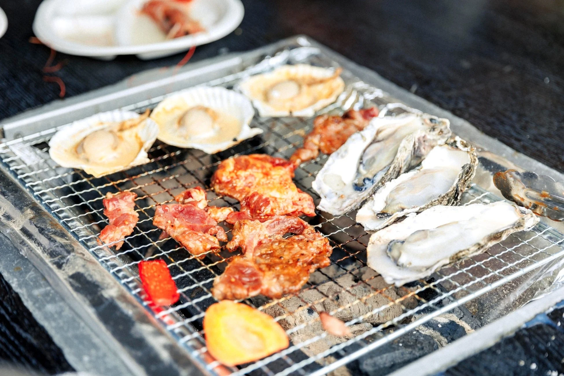 炭火のグリルでホタテ、牡蠣、肉、野菜が焼かれている様子