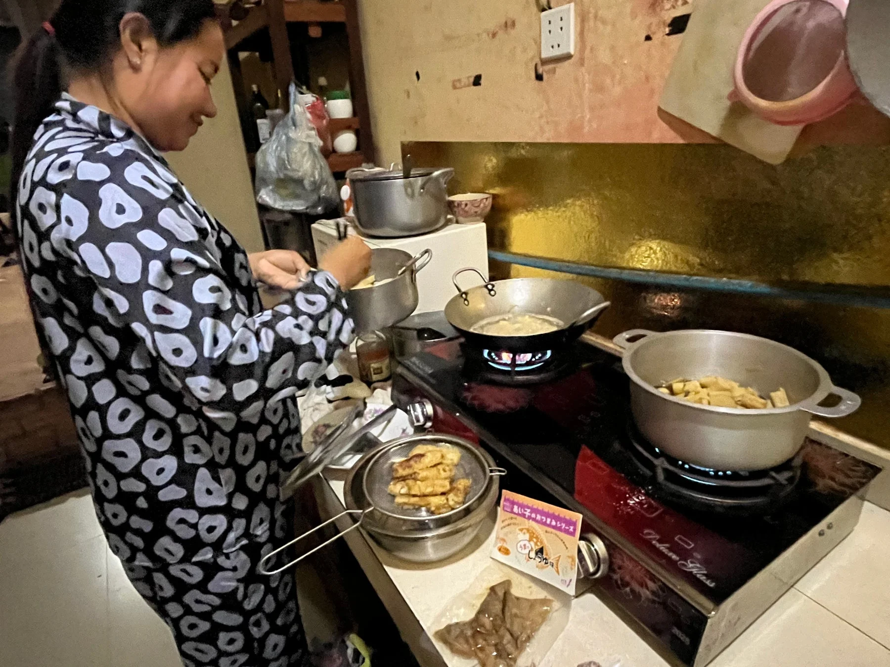 家庭のキッチンで、女性がガスコンロを使って複数の料理を同時に作っている様子