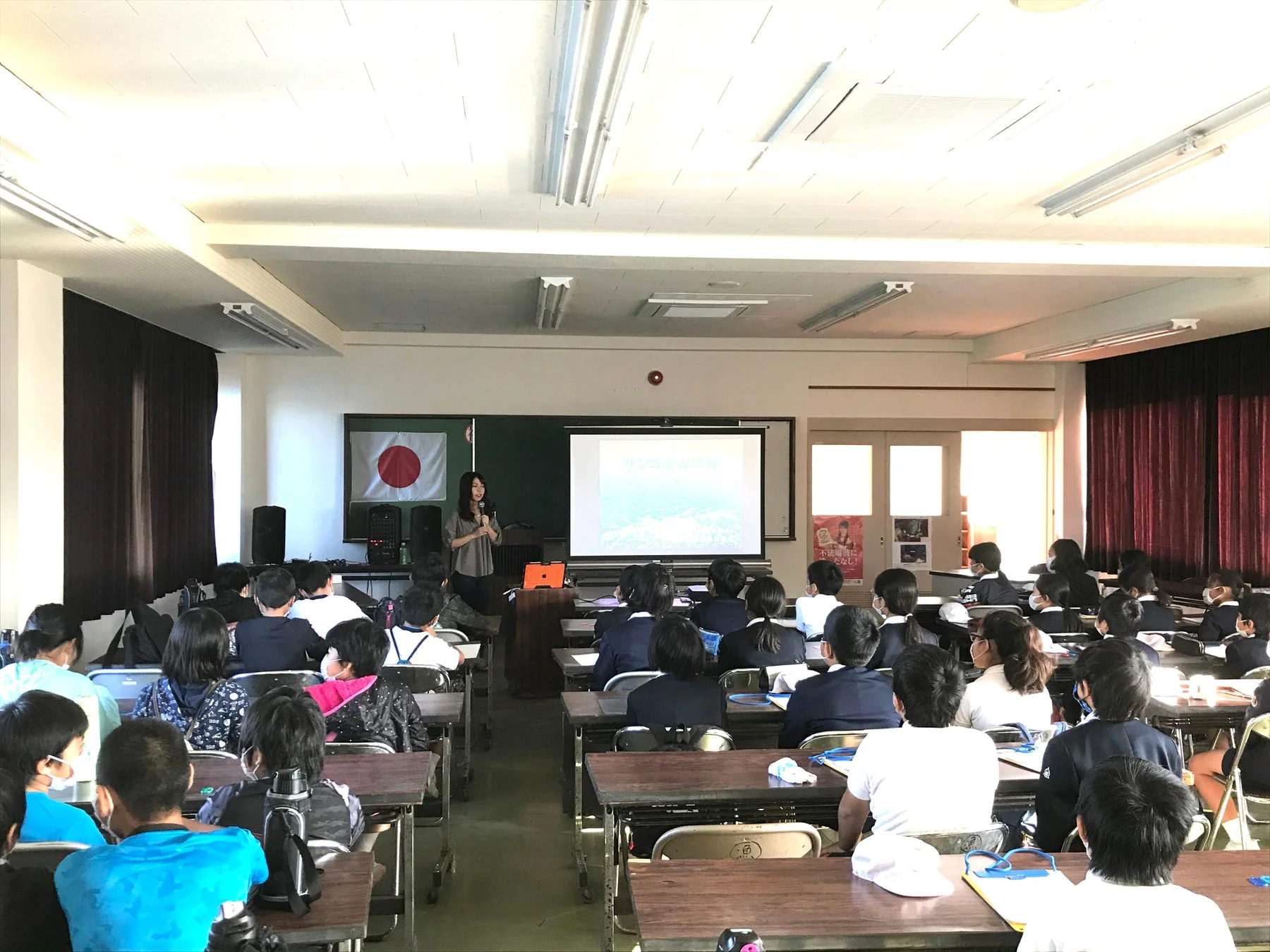 教室で女性講師が生徒たちにサンゴ礁の現状についてプレゼンテーションを行っている