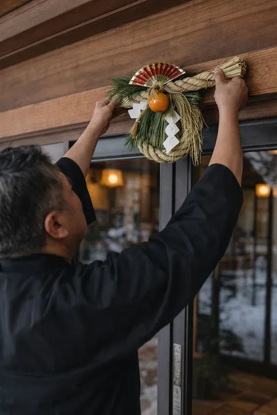 男性が木製のドア枠に日本の伝統的な正月飾りであるしめ飾りを設置している様子。新年を迎える準備をしている場面を捉えた写真です。