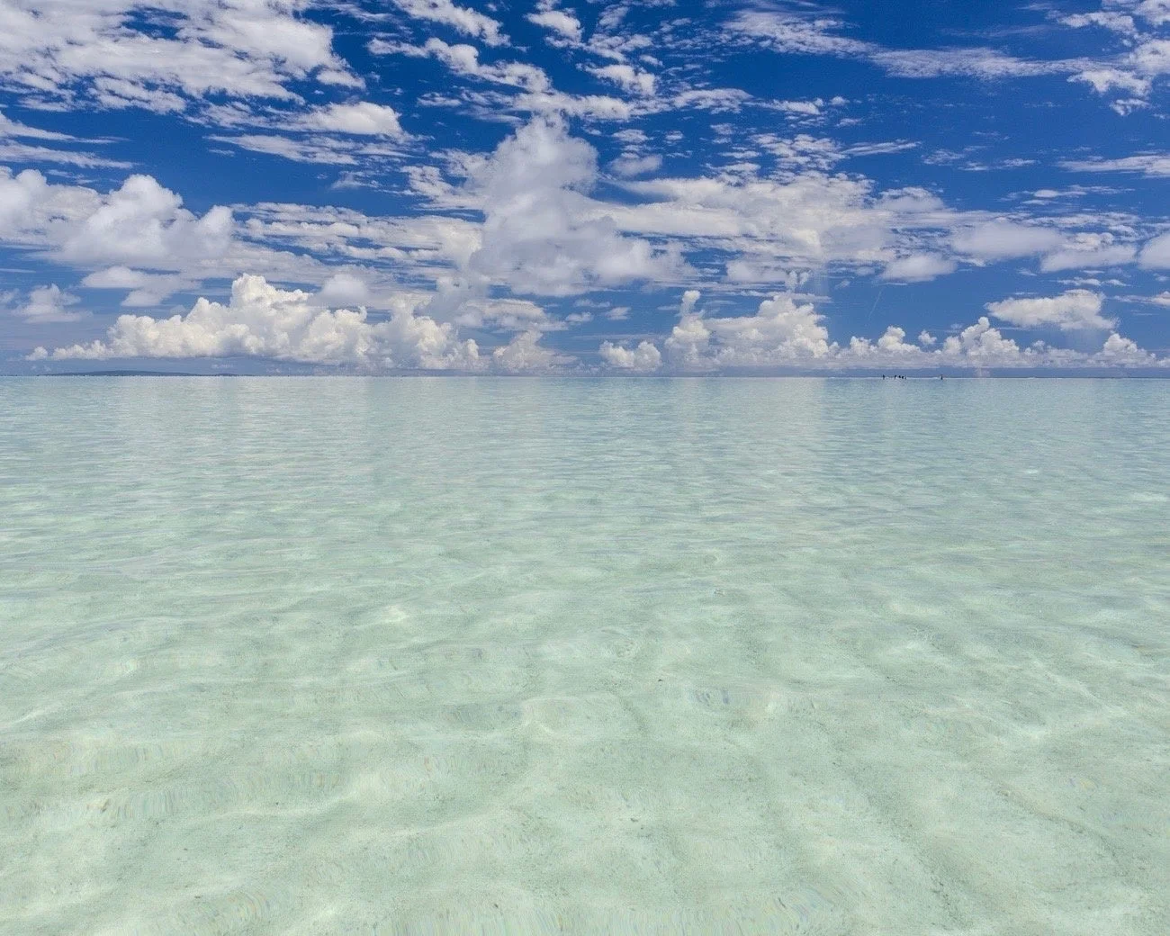 青い空に白い雲が広がる下、透き通ったエメラルドグリーンの海