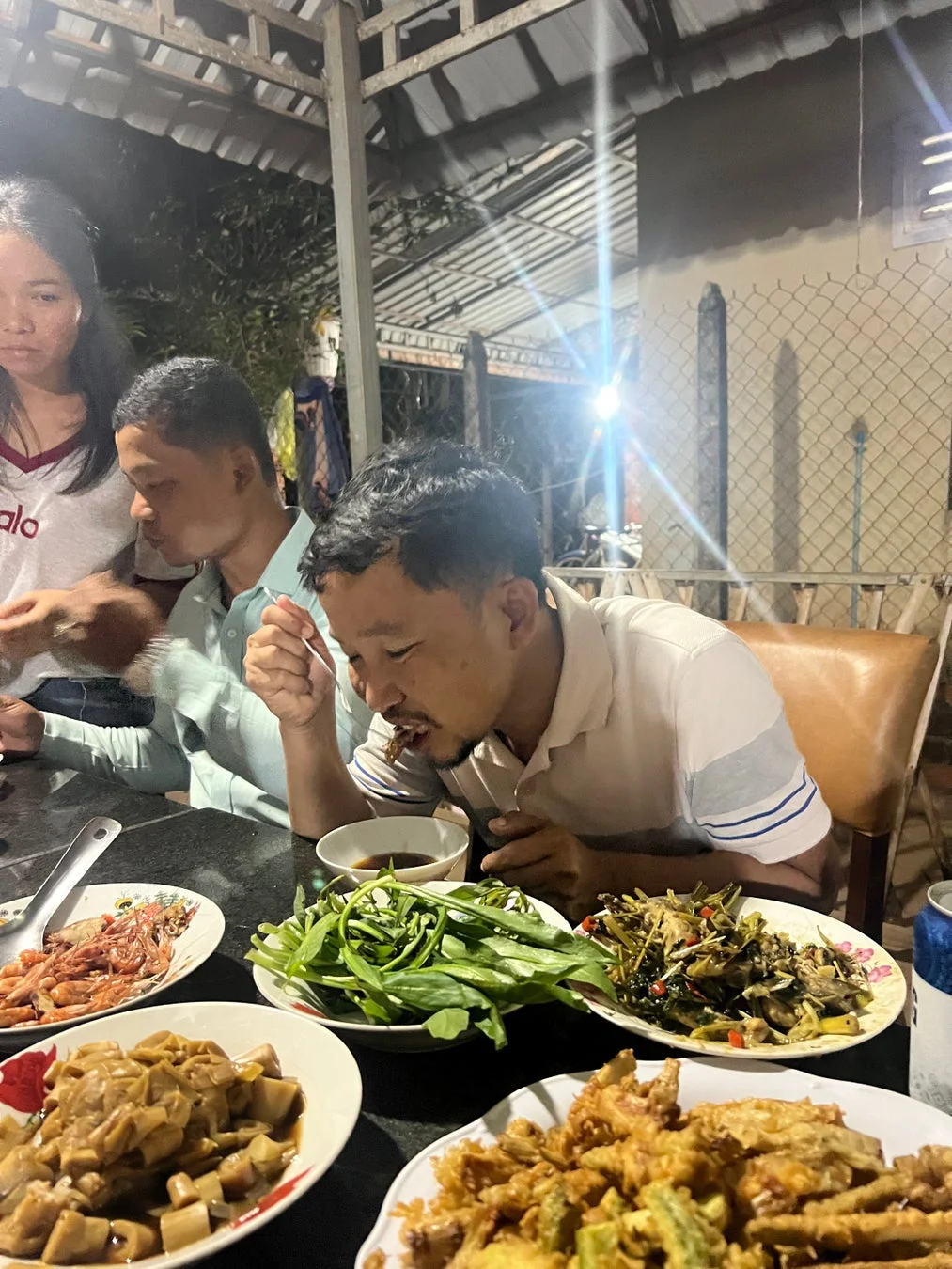 夜、屋外で数人が食卓を囲み、さまざまなアジア料理を楽しんでいる