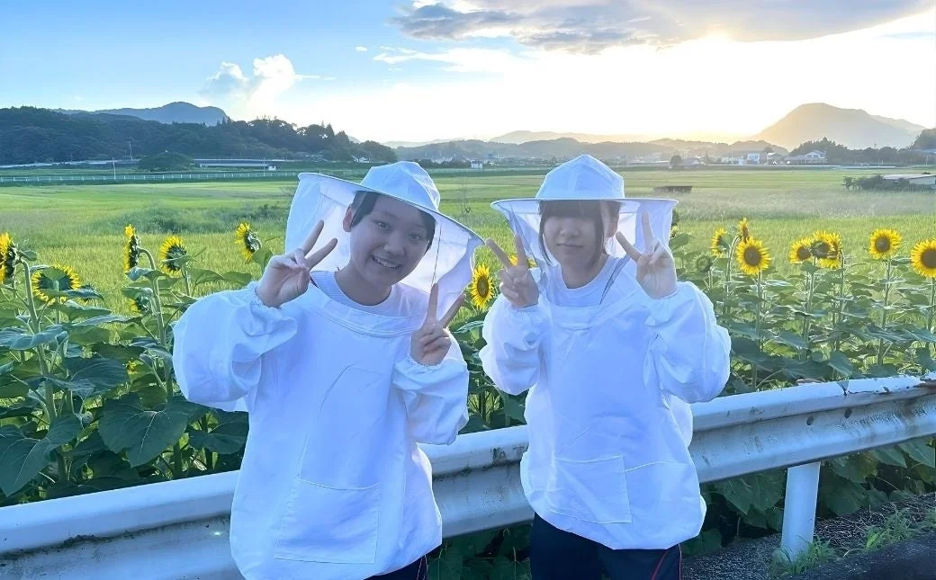 ひまわり畑でピースサインをする二人