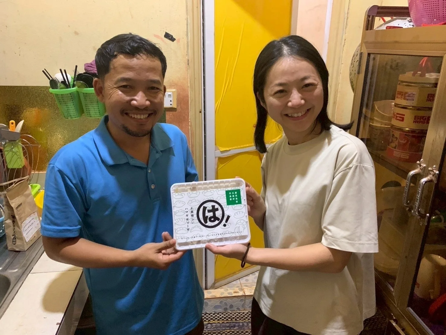 笑顔の男女が自宅のキッチンで「ハマギョーザ」のトレーを手にしている