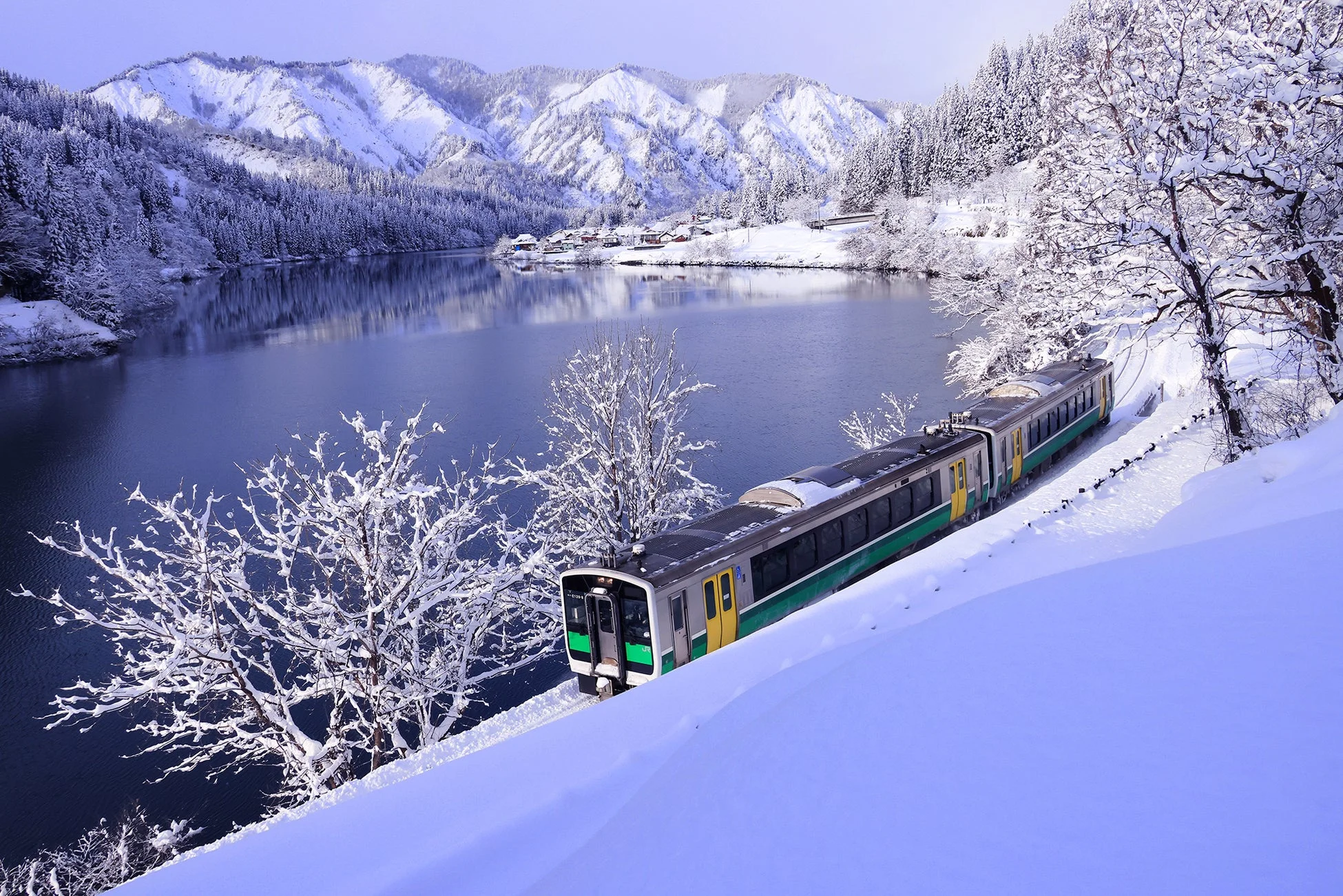 雪に覆われた山々と湖畔を走る列車