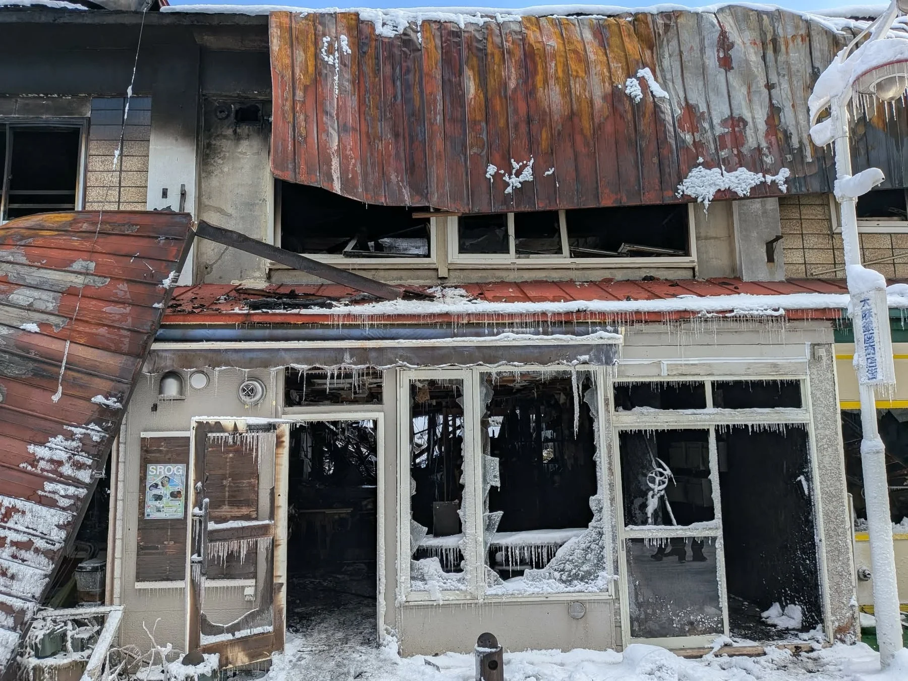 雪に覆われた火災現場の建物で、窓ガラスが割れ、内部が焼け焦げている様子