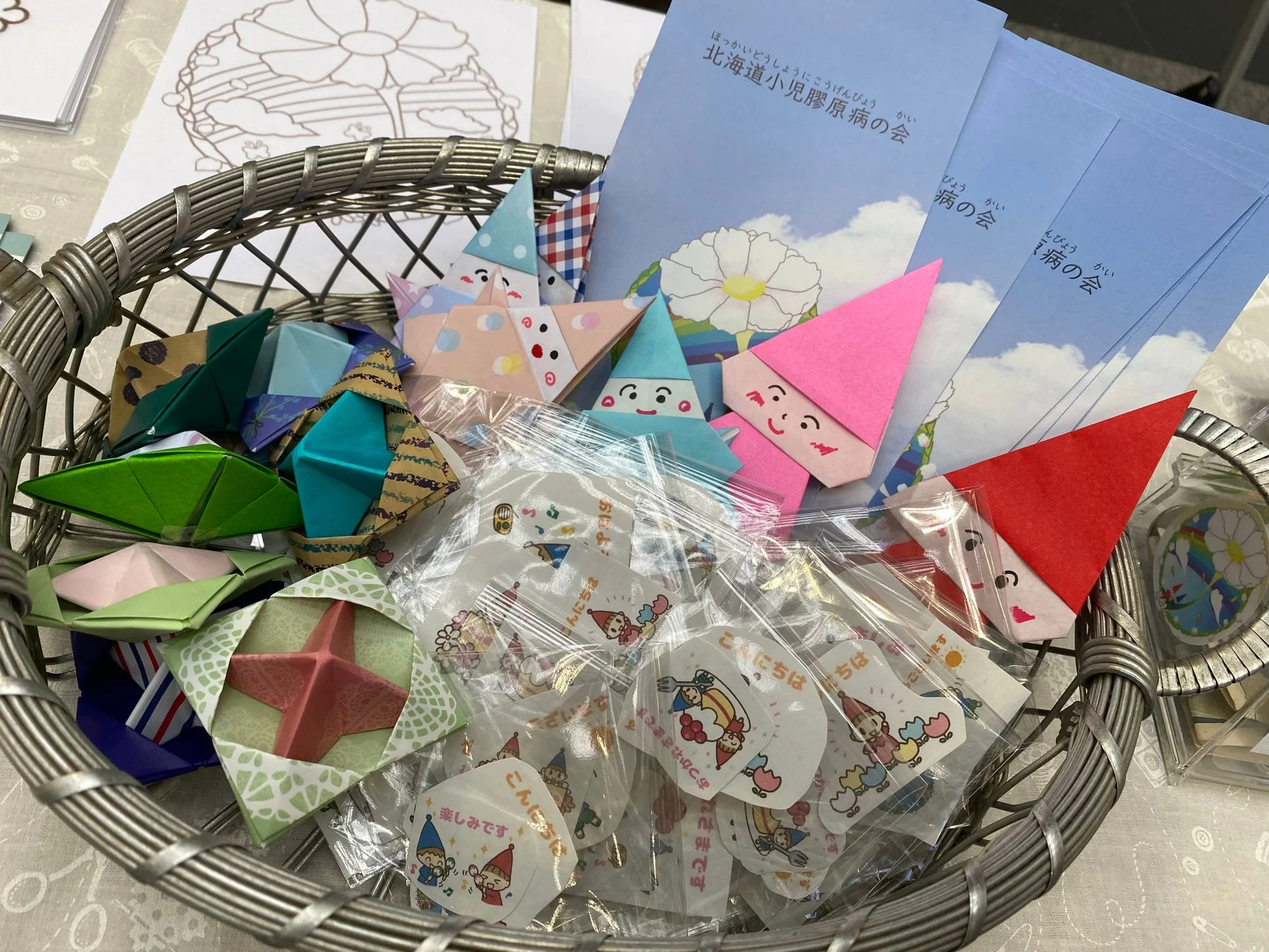銀色の籠の中に、カラフルな折り紙の小人や飾り、「北海道小児膠原病の会」と書かれたパンフレット