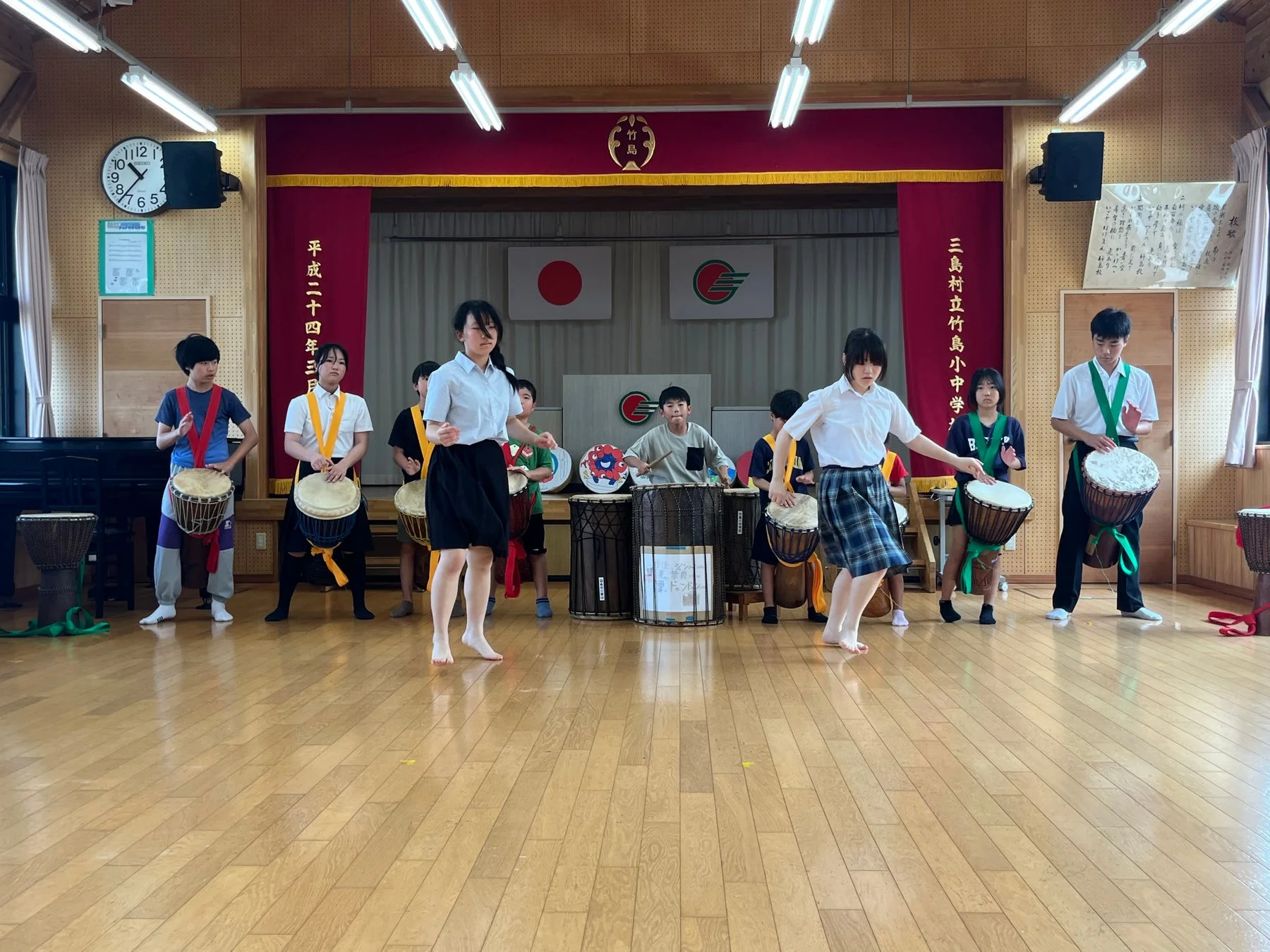 日本の学校の体育館で、小中学生たちが民族楽器のドラムを演奏している様子