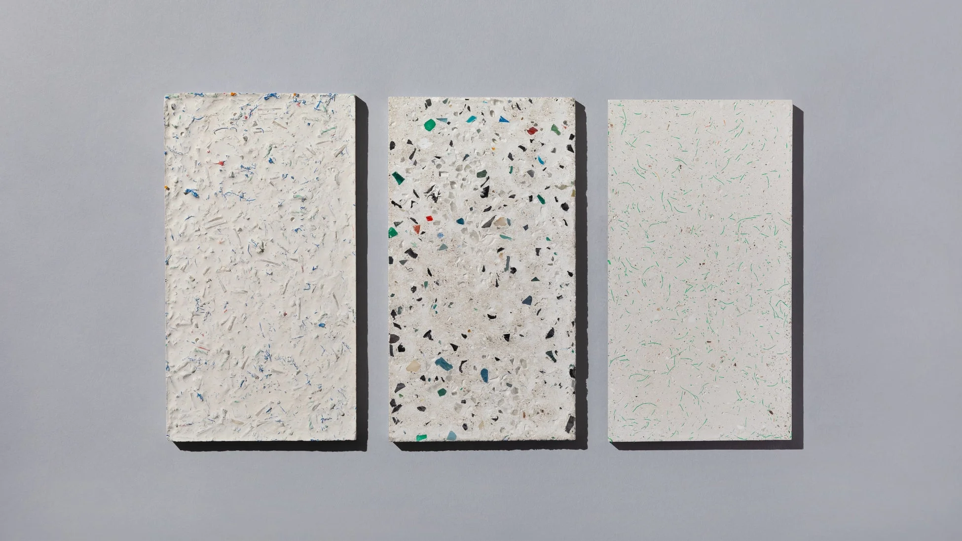 グレーの背景に、再生プラスチックや再生紙のような3種類の異なるリサイクル素材のパネルが並んでいます。独特のテクスチャと色彩が特徴で、環境配慮型素材の多様性を示しています。