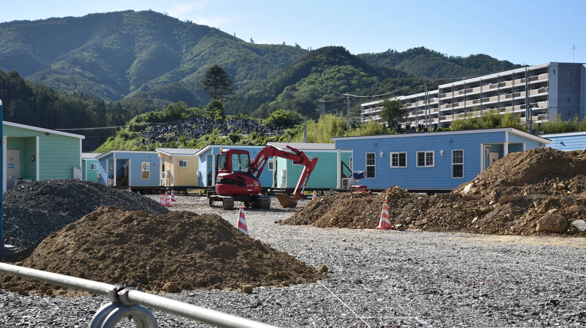 山を背景に、カラフルなプレハブ小屋が立ち並ぶ建設現場
