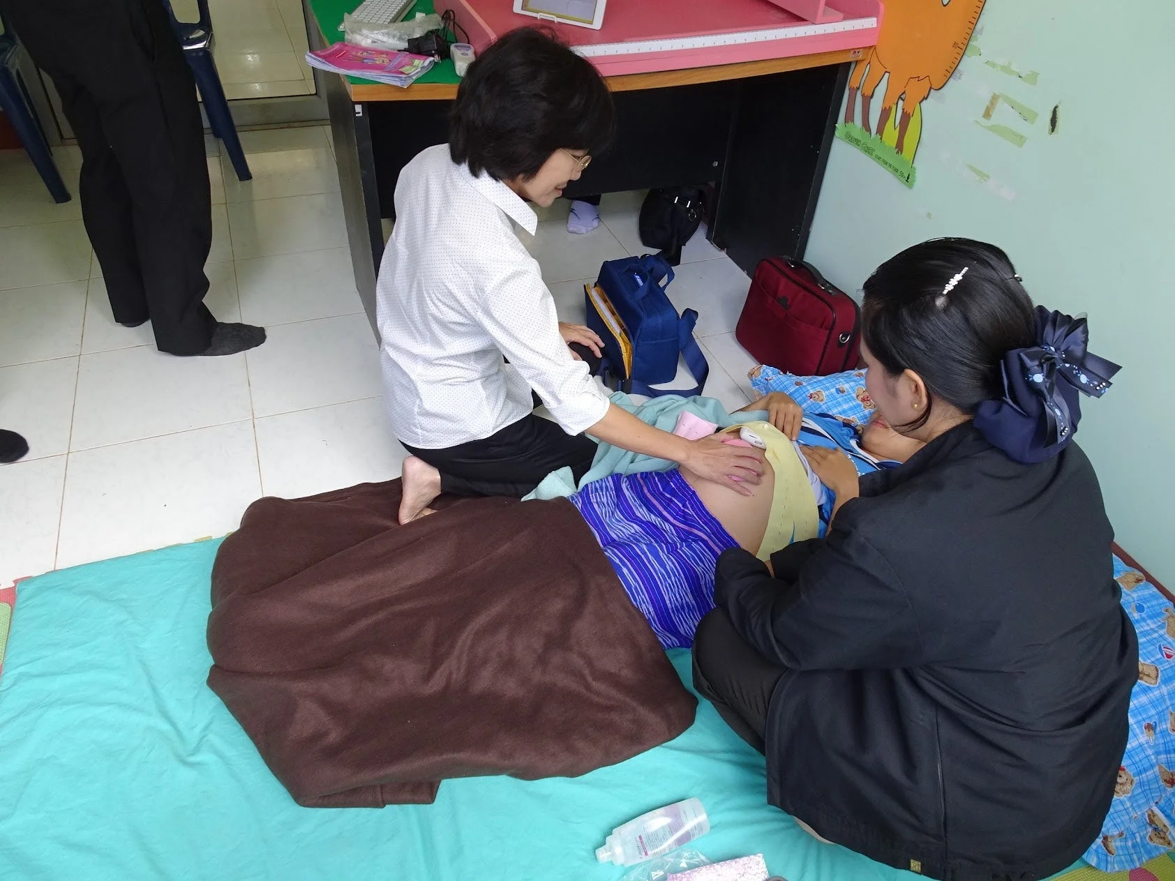 マットに横たわる人の腹部を、二人の女性が囲んで診察またはケアしている場面。