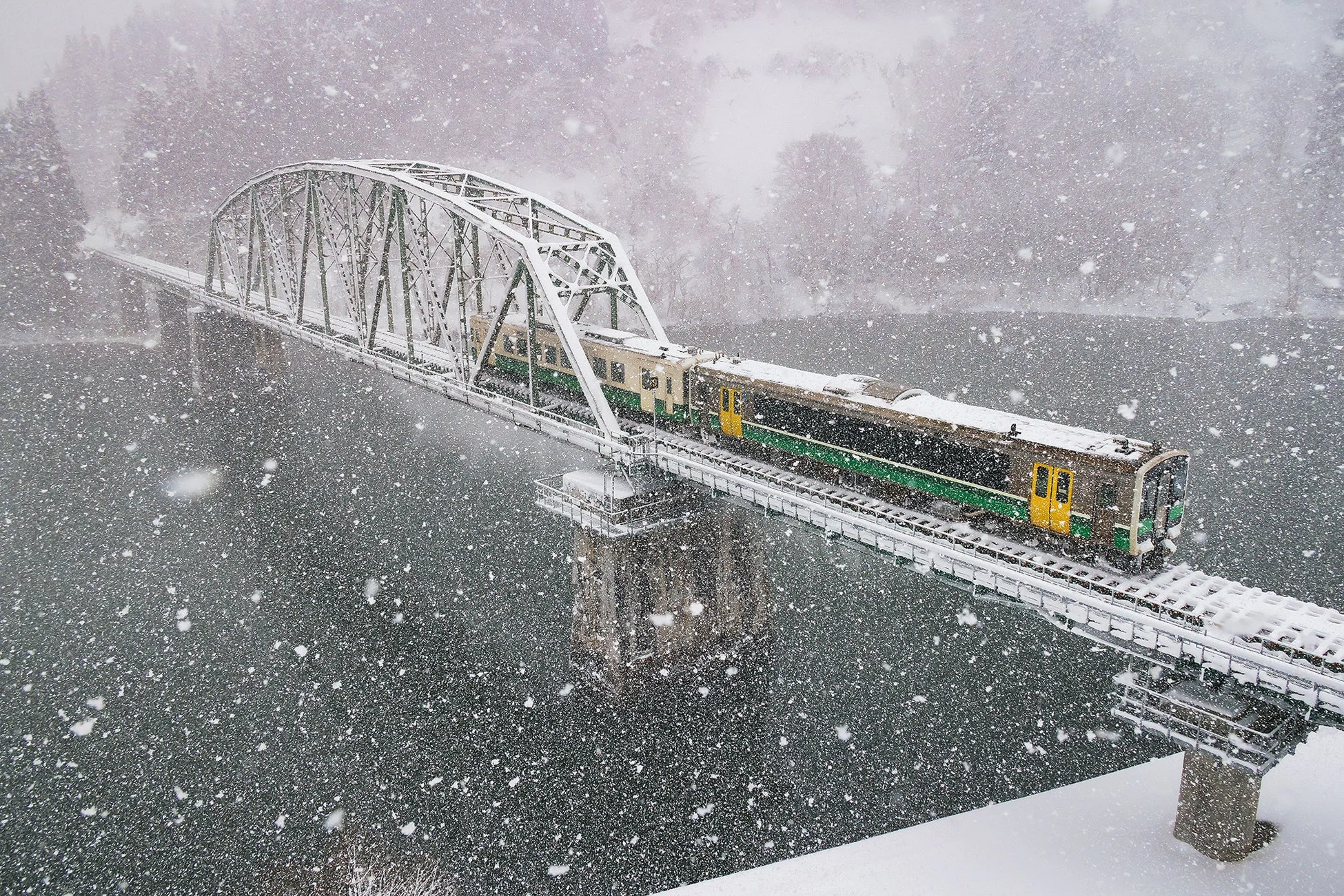 雪が激しく降る中、鉄橋を渡る列車