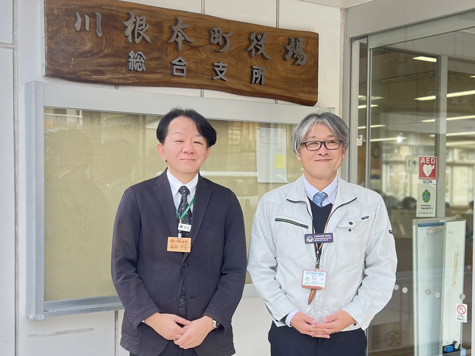 川根本町役場総合支所の建物の前で、二人の男性職員が笑顔で立っている