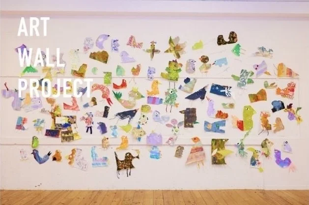 白い壁に「ART WALL PROJECT」と書かれ、カラフルな動物や抽象的な形をした多数の手作り作品が展示