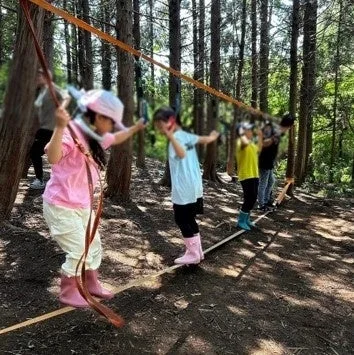 森の中でスラックラインを楽しむ子どもたち