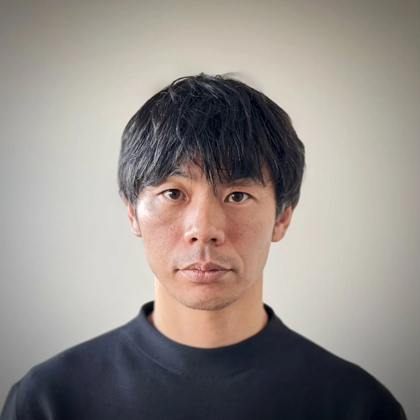 黒いハイネックの服を着た日本人男性の顔が正面から写っています