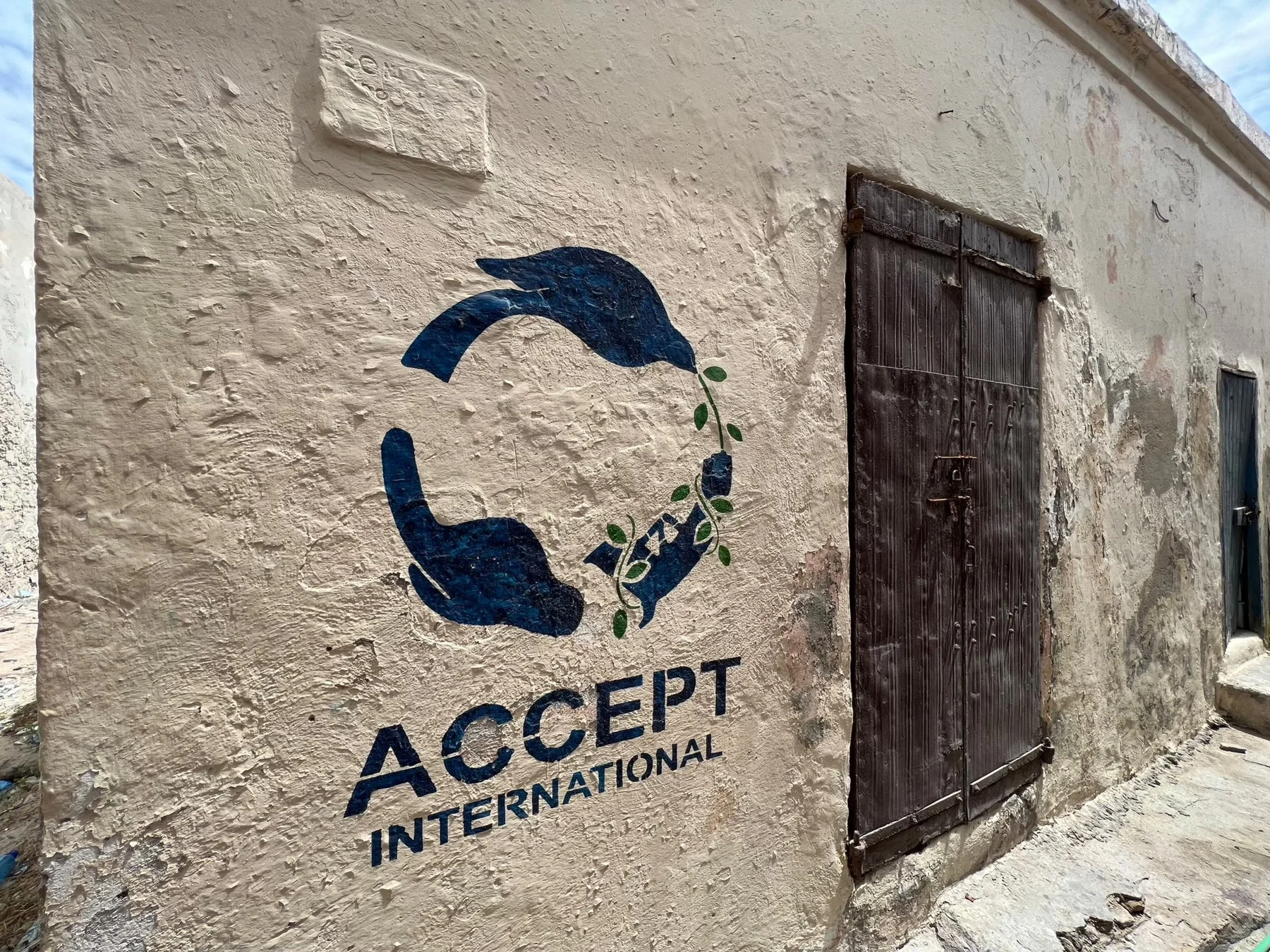 古い壁に描かれた壁画で、「ACCEPT INTERNATIONAL」の文字と、手と鳥が植物を囲む平和や環境保護を象徴するデザインが特徴です。