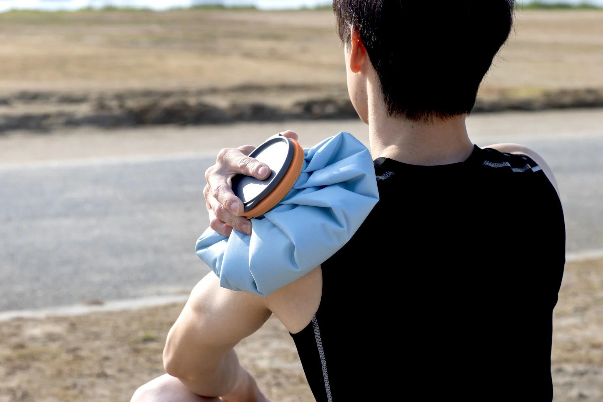 屋外で肩にアイスバッグを当てて冷却する男性