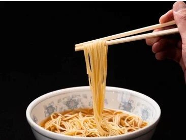 黒い背景をバックに、箸で丼から麺を高く持ち上げている様子を写した写真です。