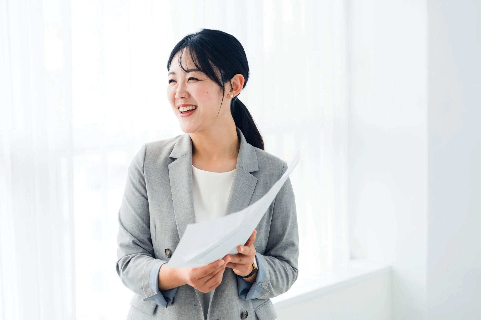 明るい白い背景の前で、笑顔で書類を手にしているビジネスウーマンのポートレート