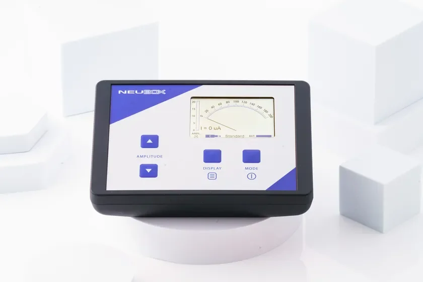 白い背景に置かれた黒い筐体の電子測定器のクローズアップ画像。ディスプレイには「NEUBOX」のロゴ、電流値、目盛りが表示され、操作ボタンが見える。