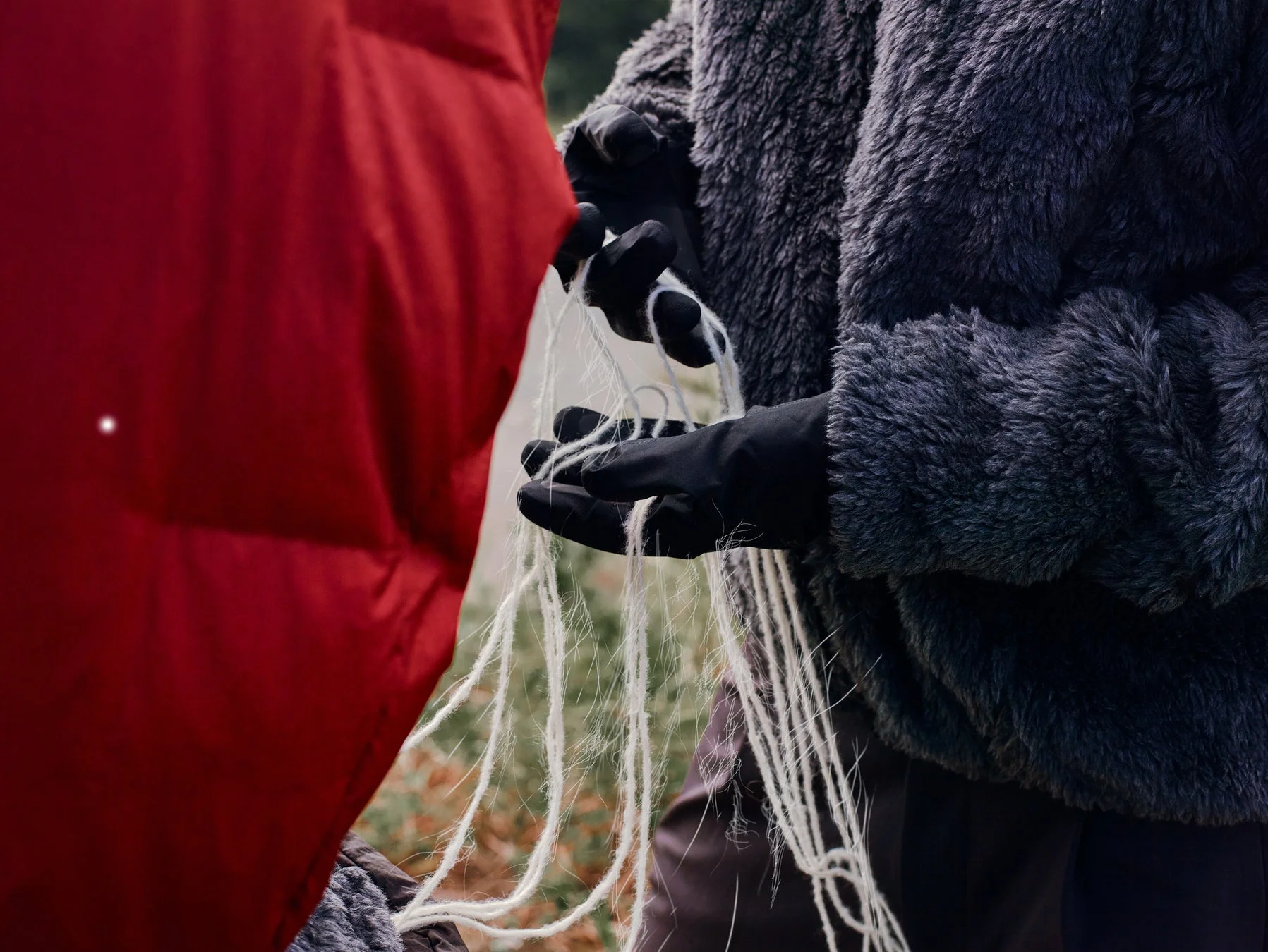 黒い手袋をはめた手が白い糸を操るクローズアップ