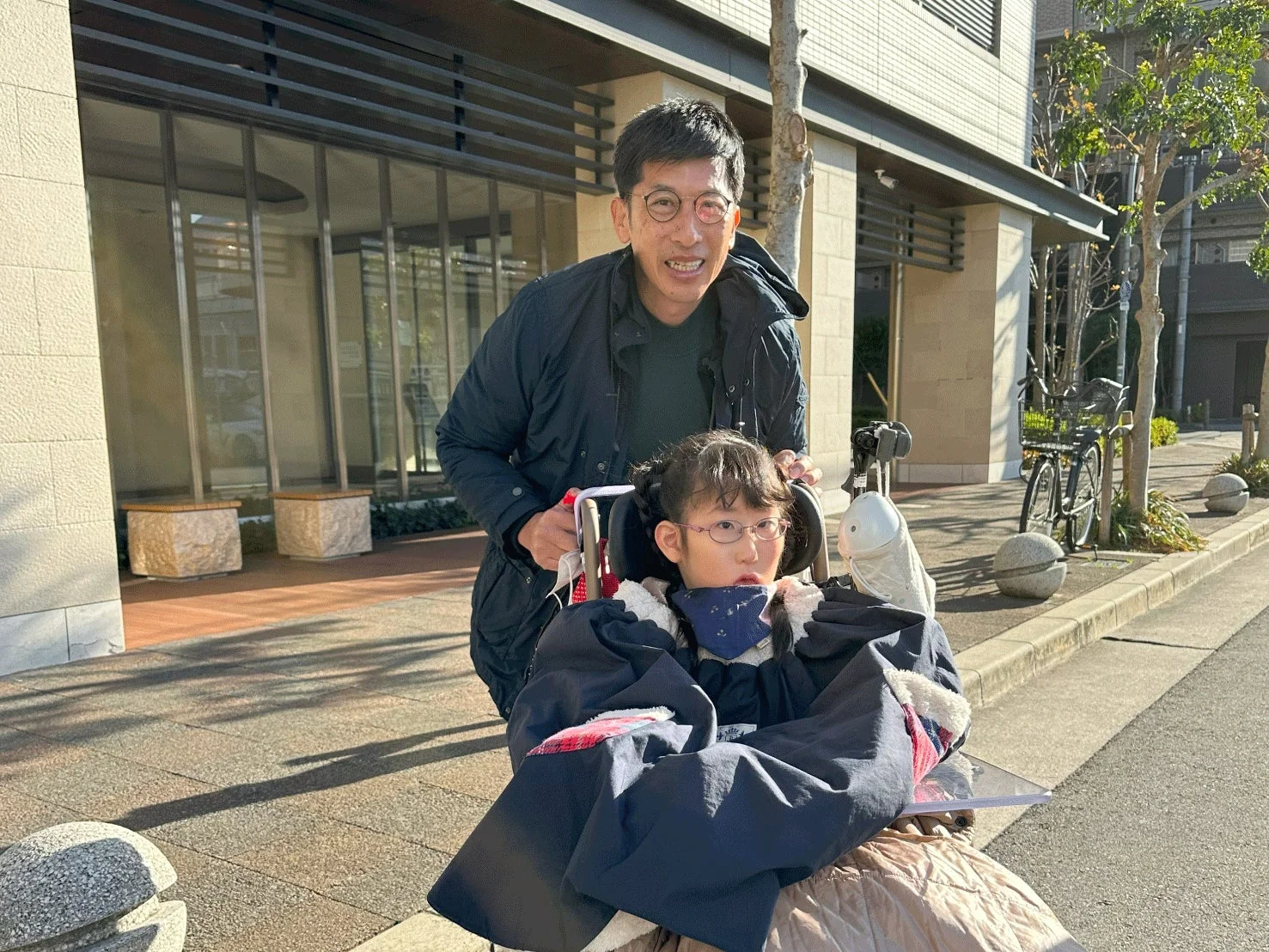 車いすの少女と男性が屋外で散歩する様子