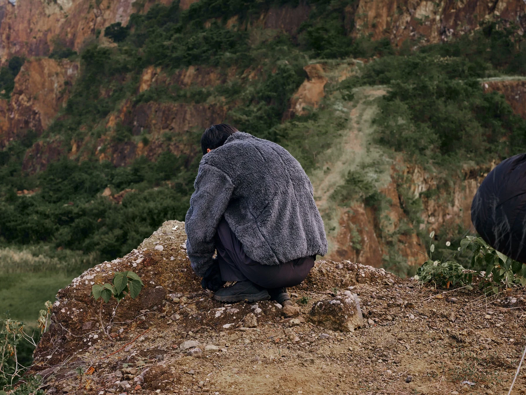 岩だらけの地面にしゃがみこむ人物のフリースジャケット姿