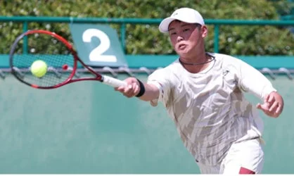 屋外のテニスコートで、若い男性選手がテニスボールをフォアハンドで打ち返している瞬間