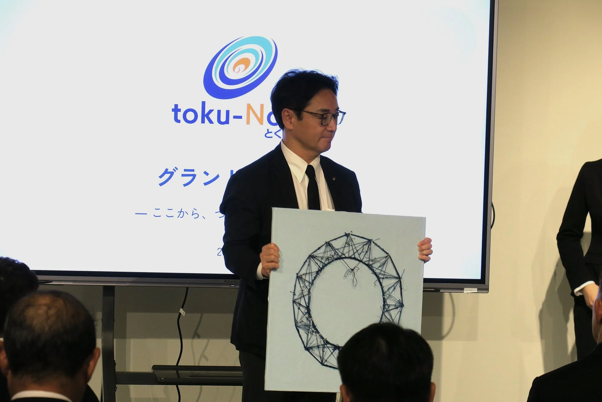 スーツ姿の男性が円形のオブジェを掲げるビジネスイベント